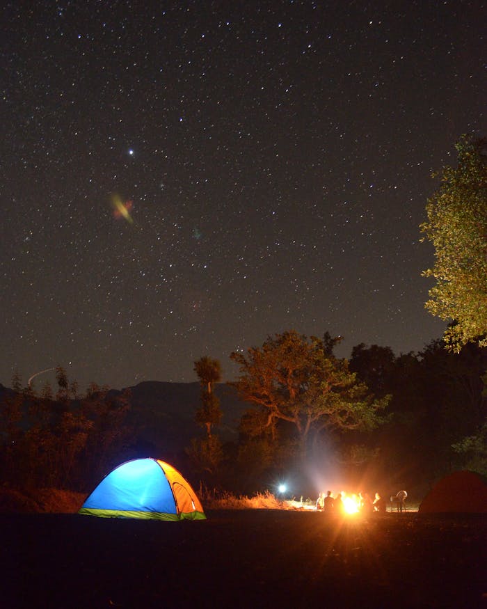 Outdoor camping under a starry night sky with a glowing tent and campfire.